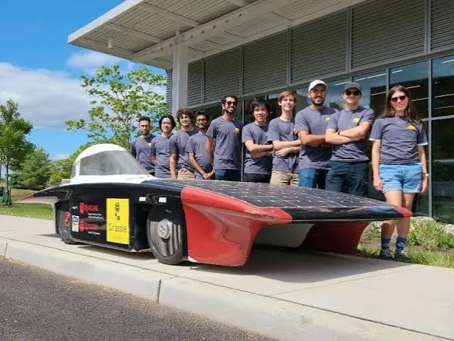 The Rutgers Solar Car team posing beside the solar car outside a building.
